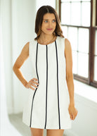 Woman wearing a white dress with black lines in a bright room.