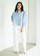 Woman wearing a blue patterned blouse and white pants against a white background