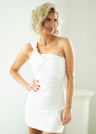 Woman wearing a white one-shoulder dress against a plain background