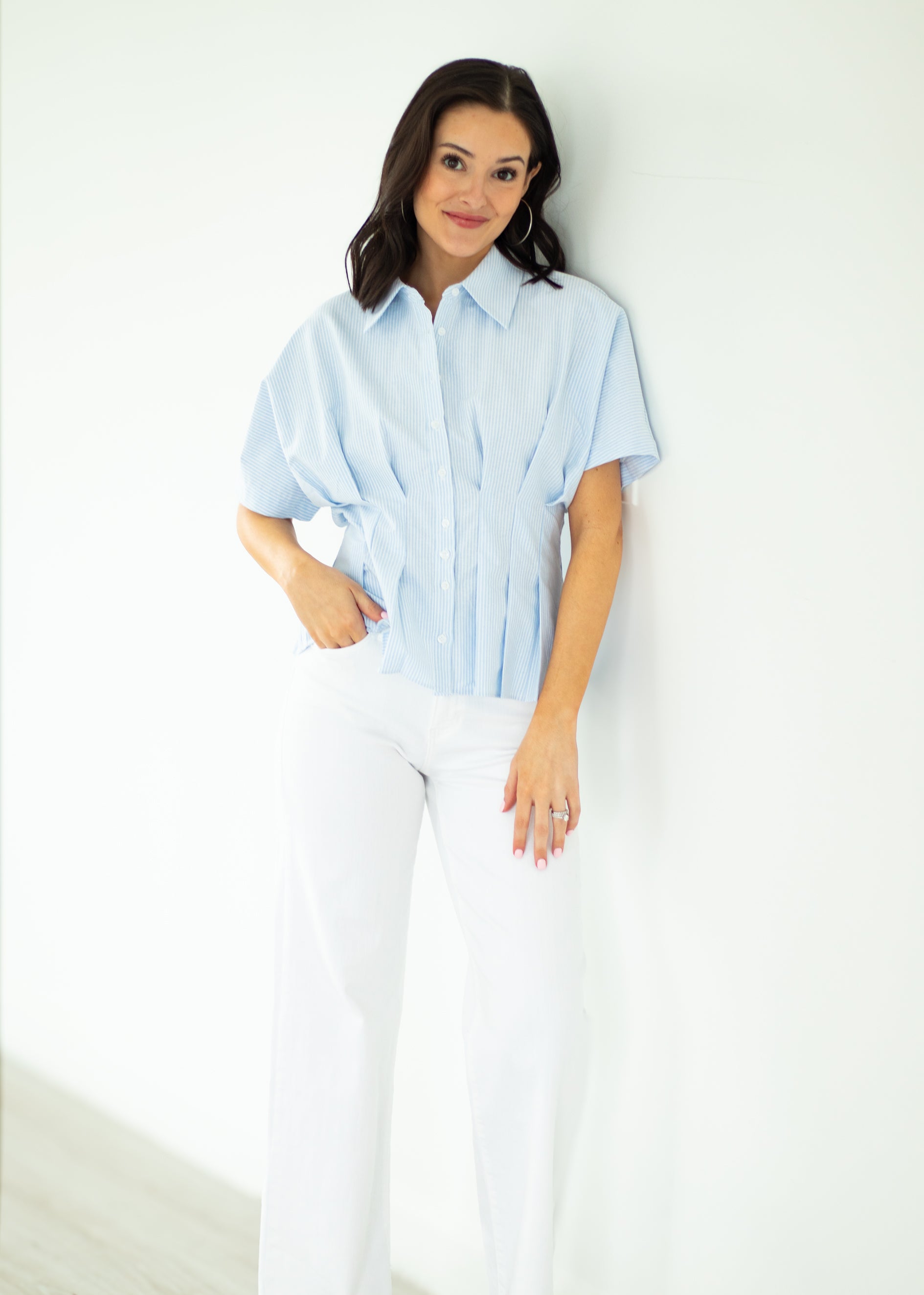 Woman wearing a light blue shirt and white pants against a white background