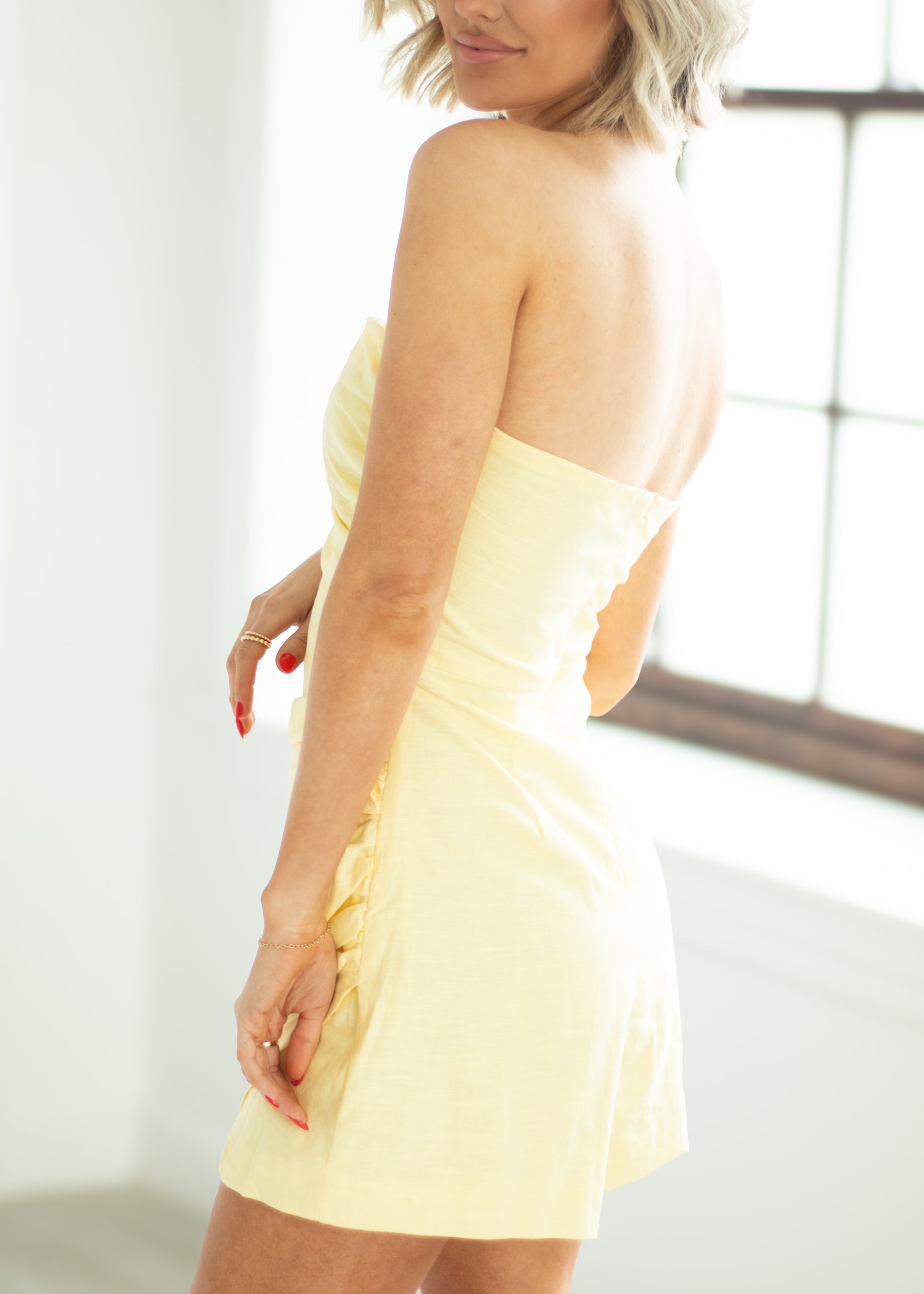 Woman wearing a yellow strapless dress in a bright room.