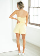Woman wearing a yellow strapless romper in a minimal indoor setting