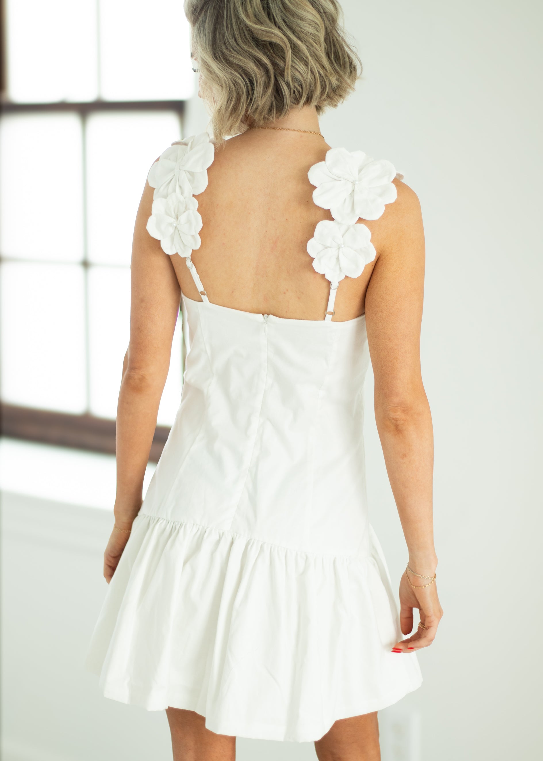 White dress with floral straps worn by a person in a bright room.
