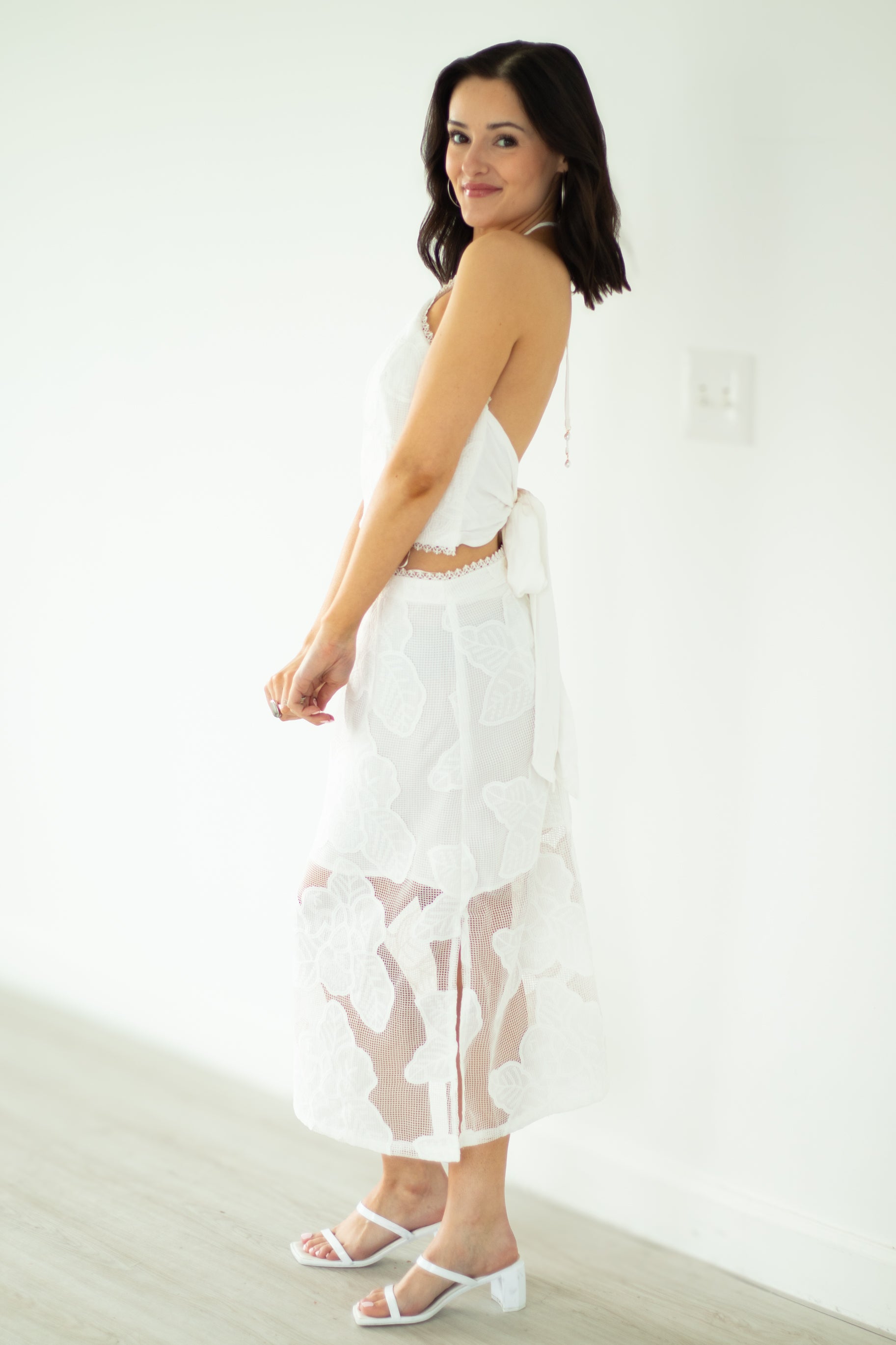 Woman wearing a white dress with sheer panels against a plain background
