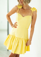 Woman wearing a yellow dress with floral straps against a white background