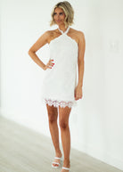Woman wearing a white halter neck dress with lace details on a plain background