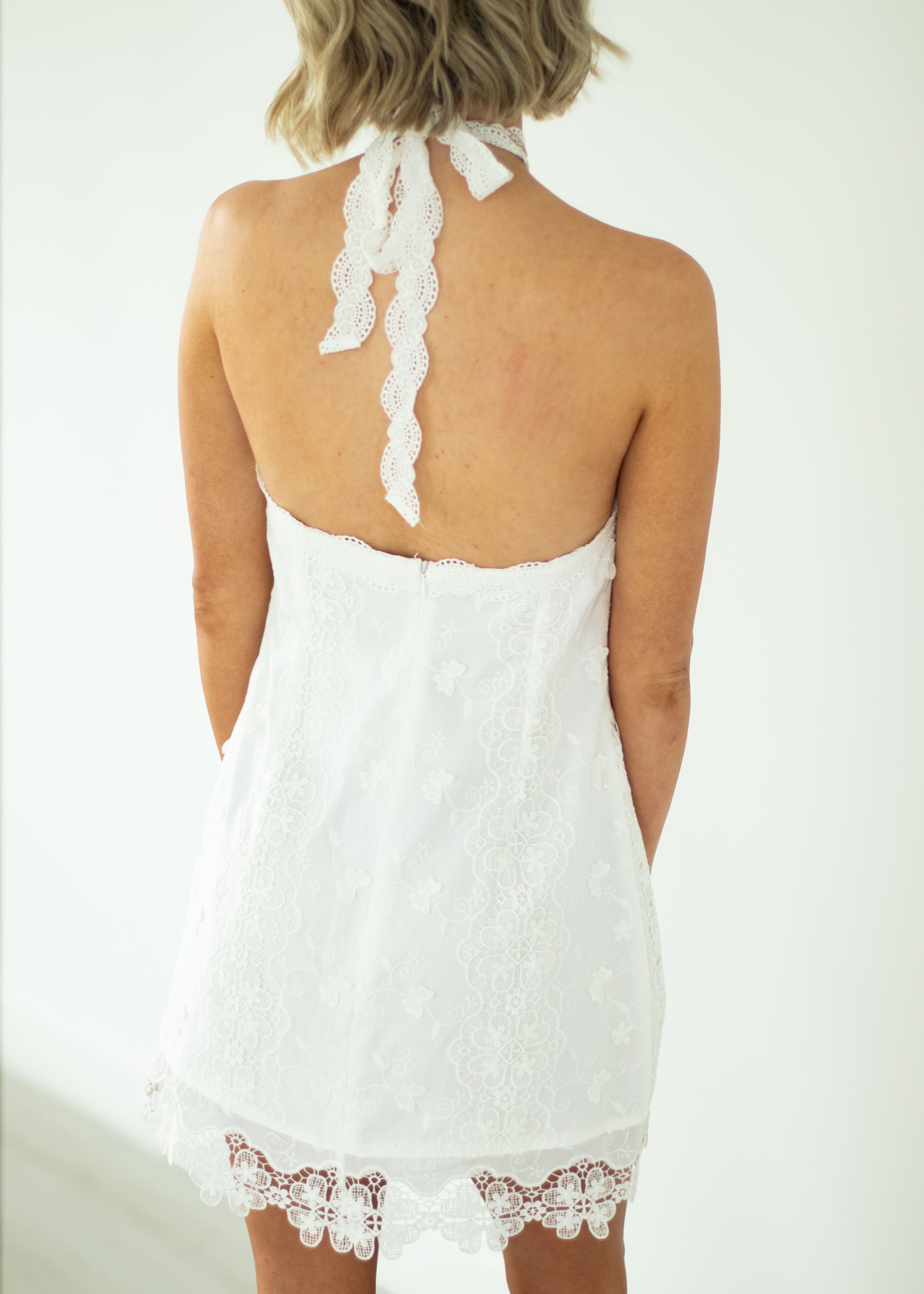 White lace dress with a halter neck design on a plain background