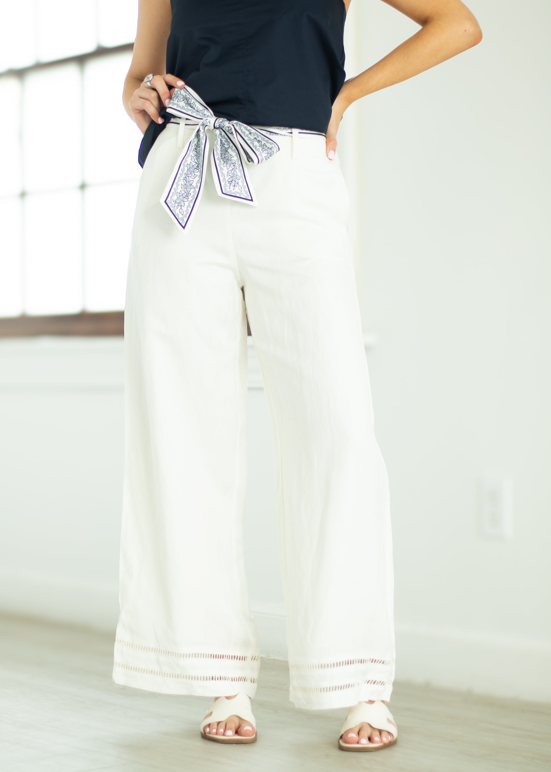 Person wearing white wide-leg pants with a navy top and decorative ribbon, standing against a light background.