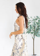 Woman wearing a floral dress with a white background and a plant in the corner