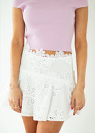 Person wearing a light purple top and white lace skirt on a white background