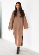 Woman wearing a long brown sweater dress against a white background