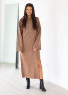 Woman wearing a long brown sweater dress with a slit on a white background