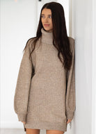 Woman wearing a beige sweater dress against a white background