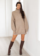 Woman wearing a beige sweater dress and brown boots against a white background