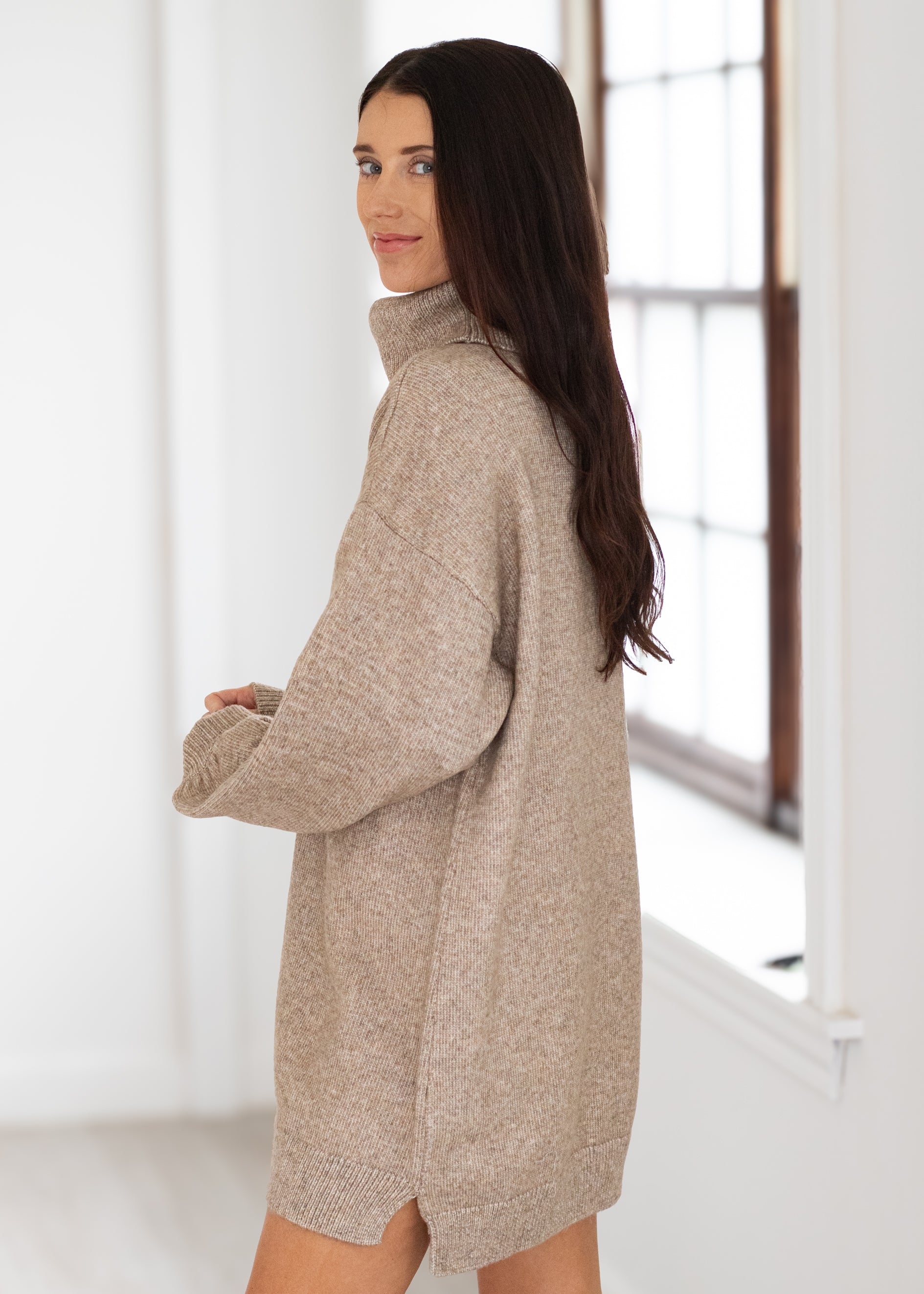 Woman wearing a beige sweater dress in a bright room