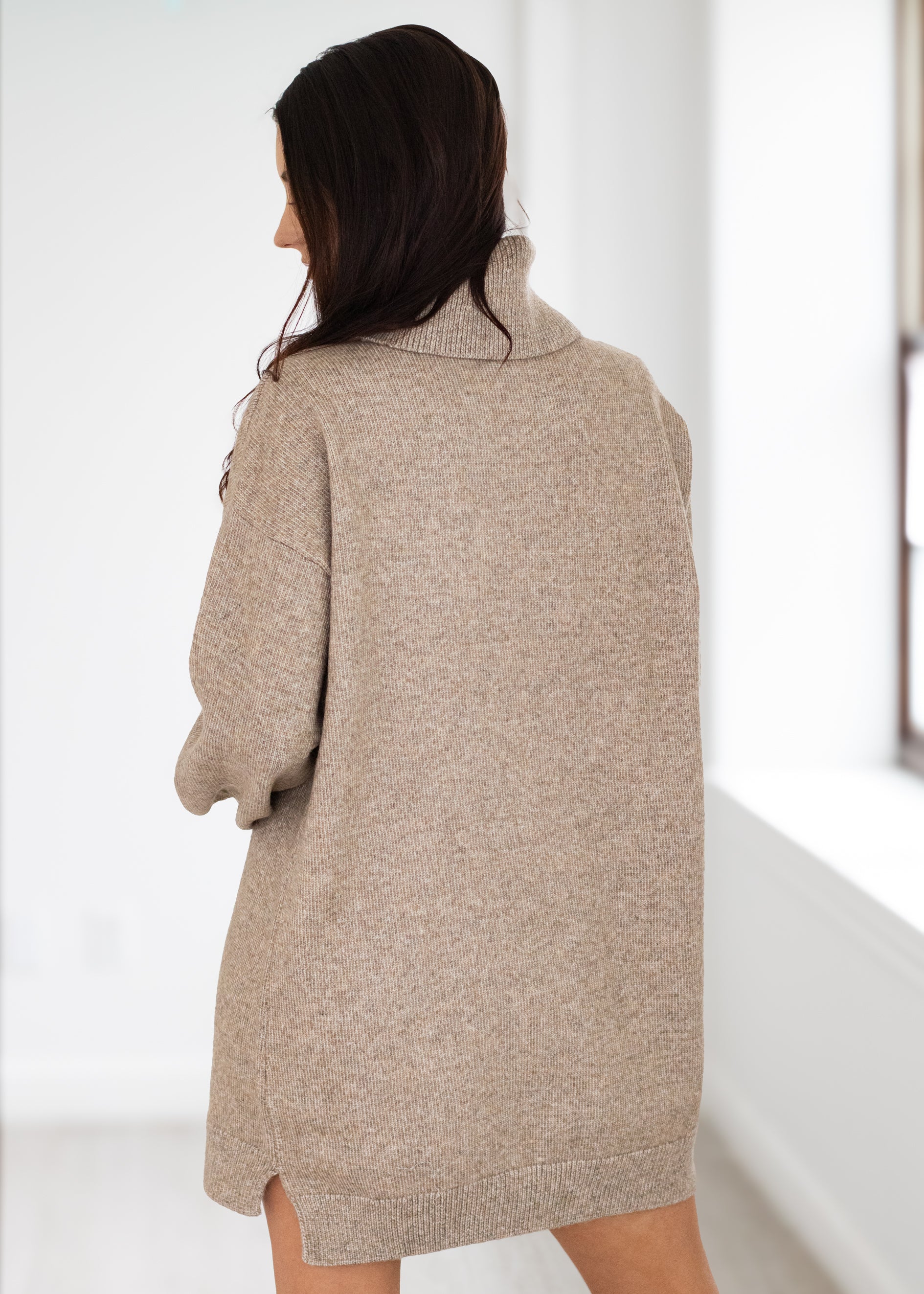 Woman wearing a beige sweater dress against a white background