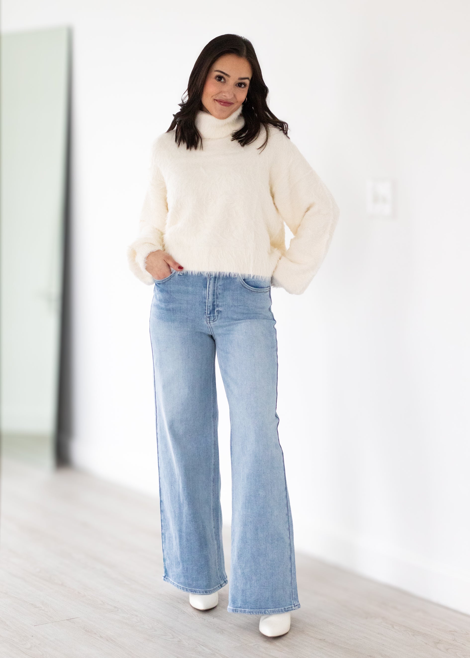 Woman wearing a cream sweater and light blue jeans in a minimalistic setting