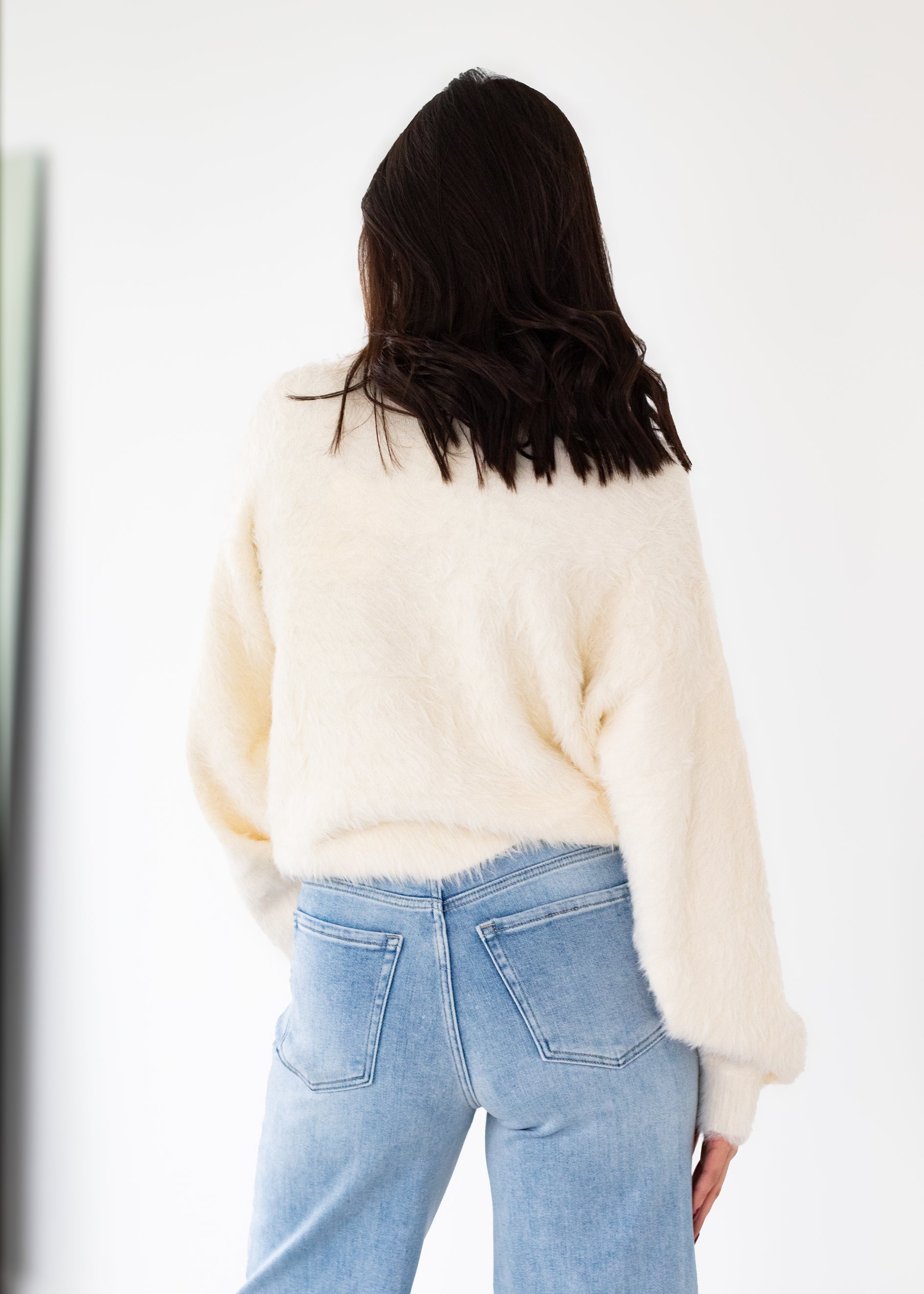 Person wearing a cream sweater and light blue jeans against a white background
