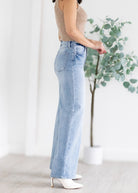 Person wearing light blue jeans with a neutral background and plant