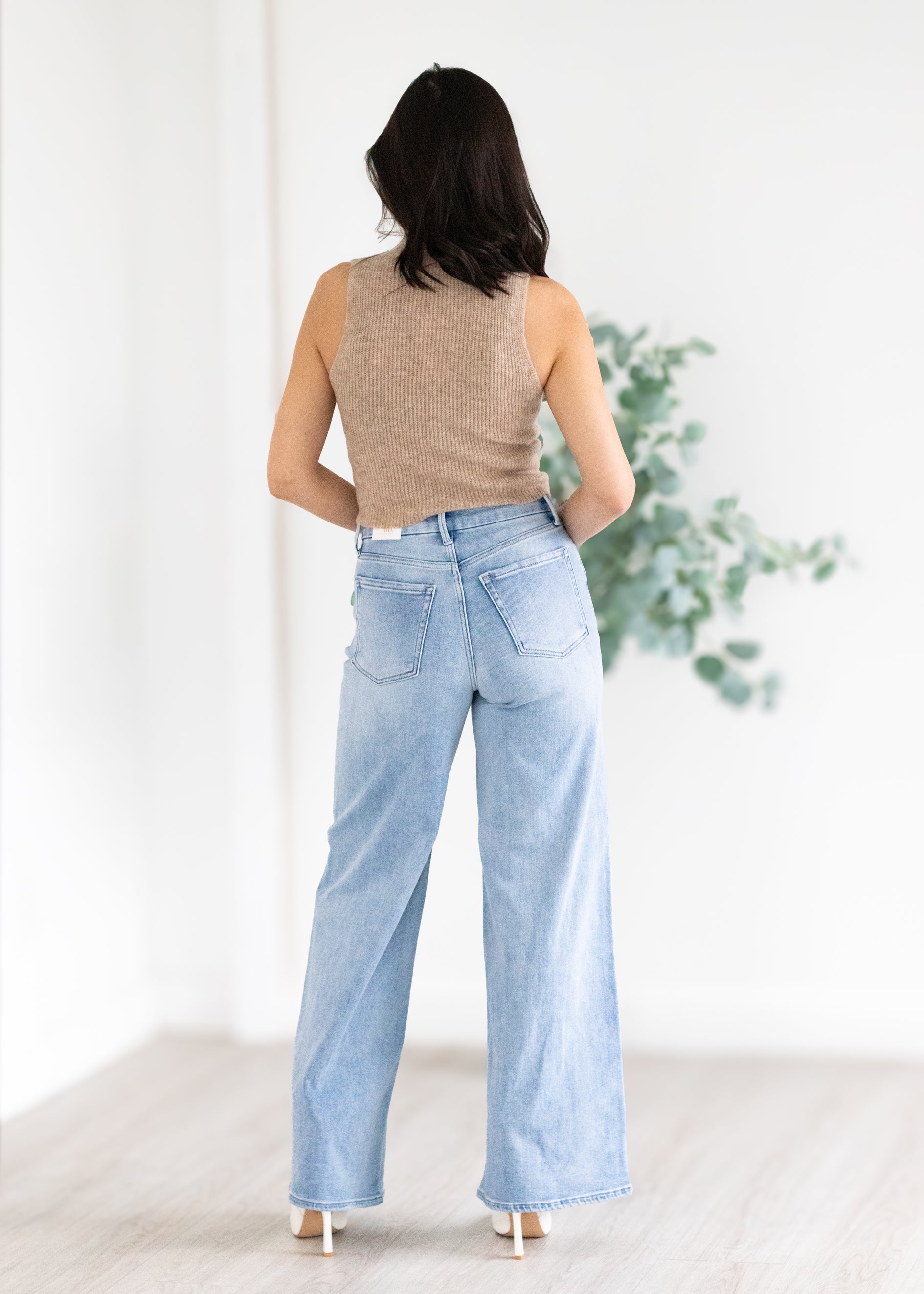 Woman wearing a beige sleeveless top and light blue jeans against a white background