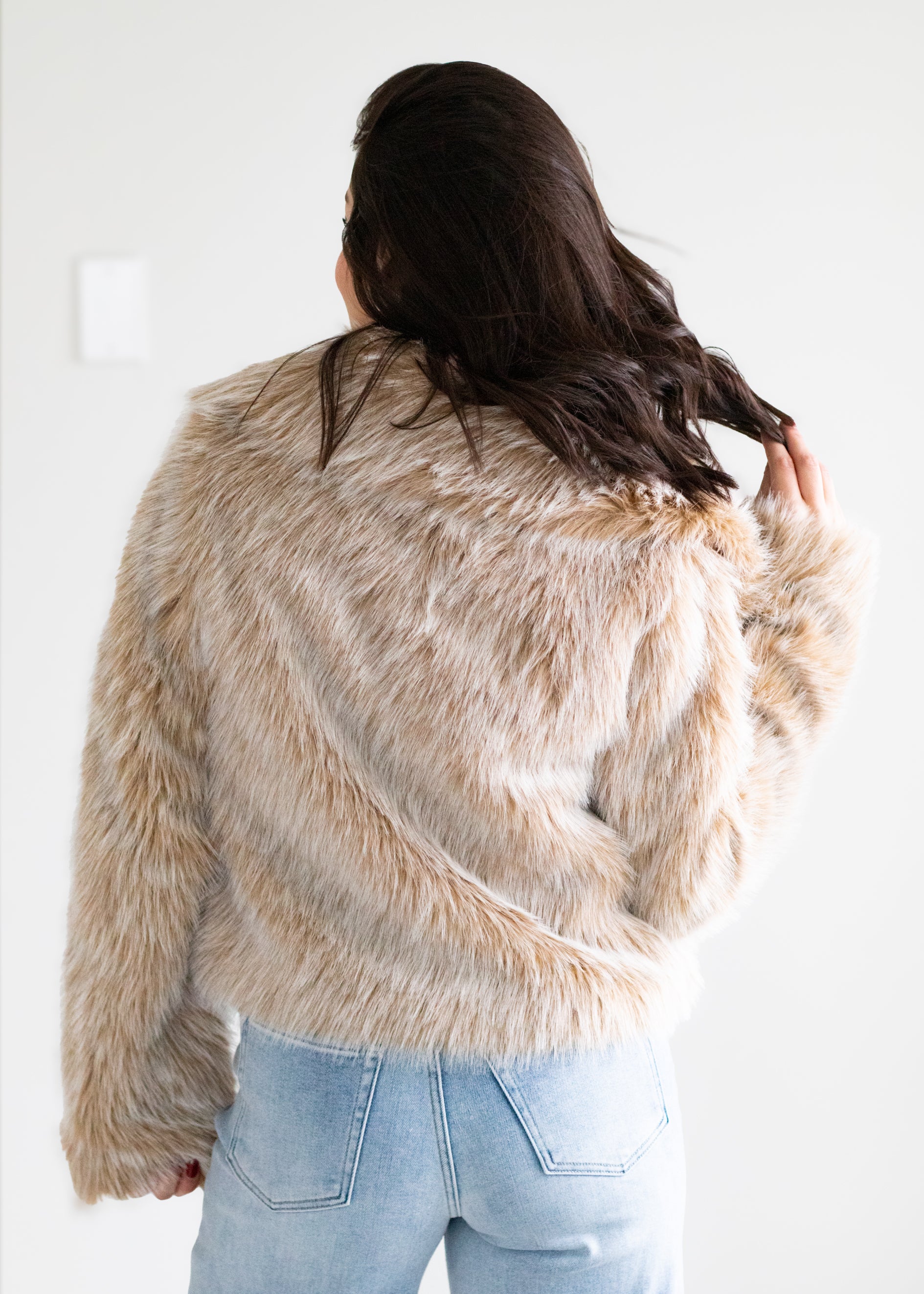 Person wearing a fluffy beige jacket against a white background