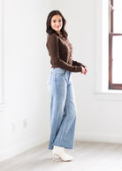 Woman wearing a brown top and blue jeans standing in a bright room.
