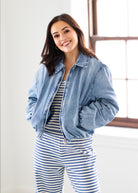 Woman wearing a denim jacket over a striped outfit in a bright room.