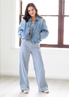 Woman wearing a denim jacket and blue and white striped pants standing in a bright room.