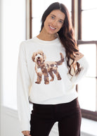 Woman wearing a white sweatshirt with a brown dog graphic, standing indoors.