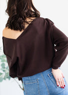 Person wearing a brown off-shoulder top and blue jeans with a blurred background