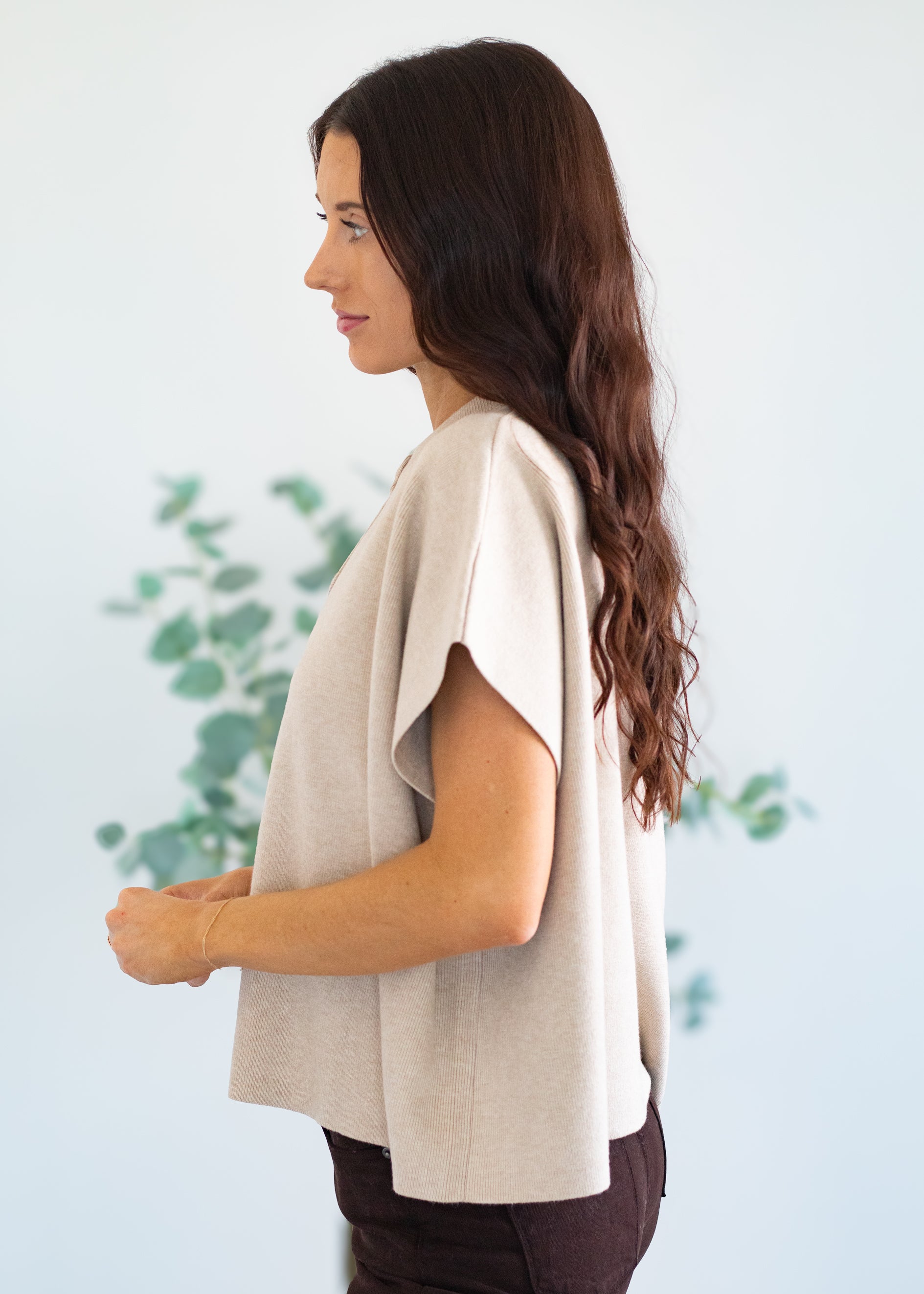 Woman wearing a beige top with a white background and greenery
