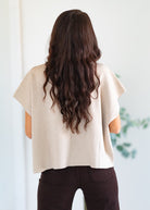 Person wearing a beige top with long, wavy hair, standing against a light background.