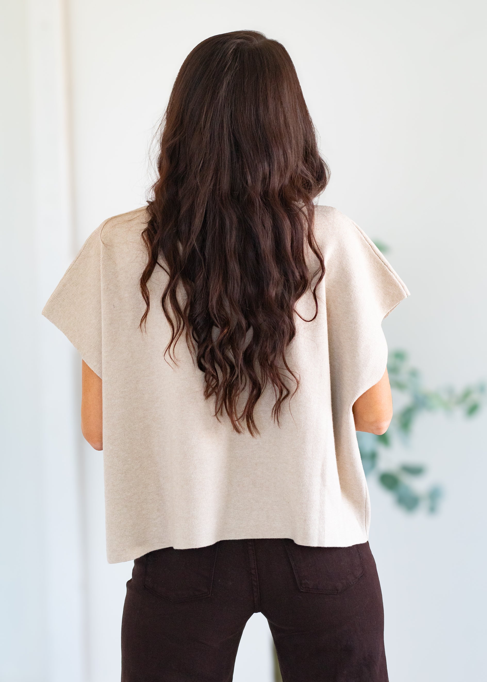 Person wearing a beige top with long, wavy hair, standing against a light background.