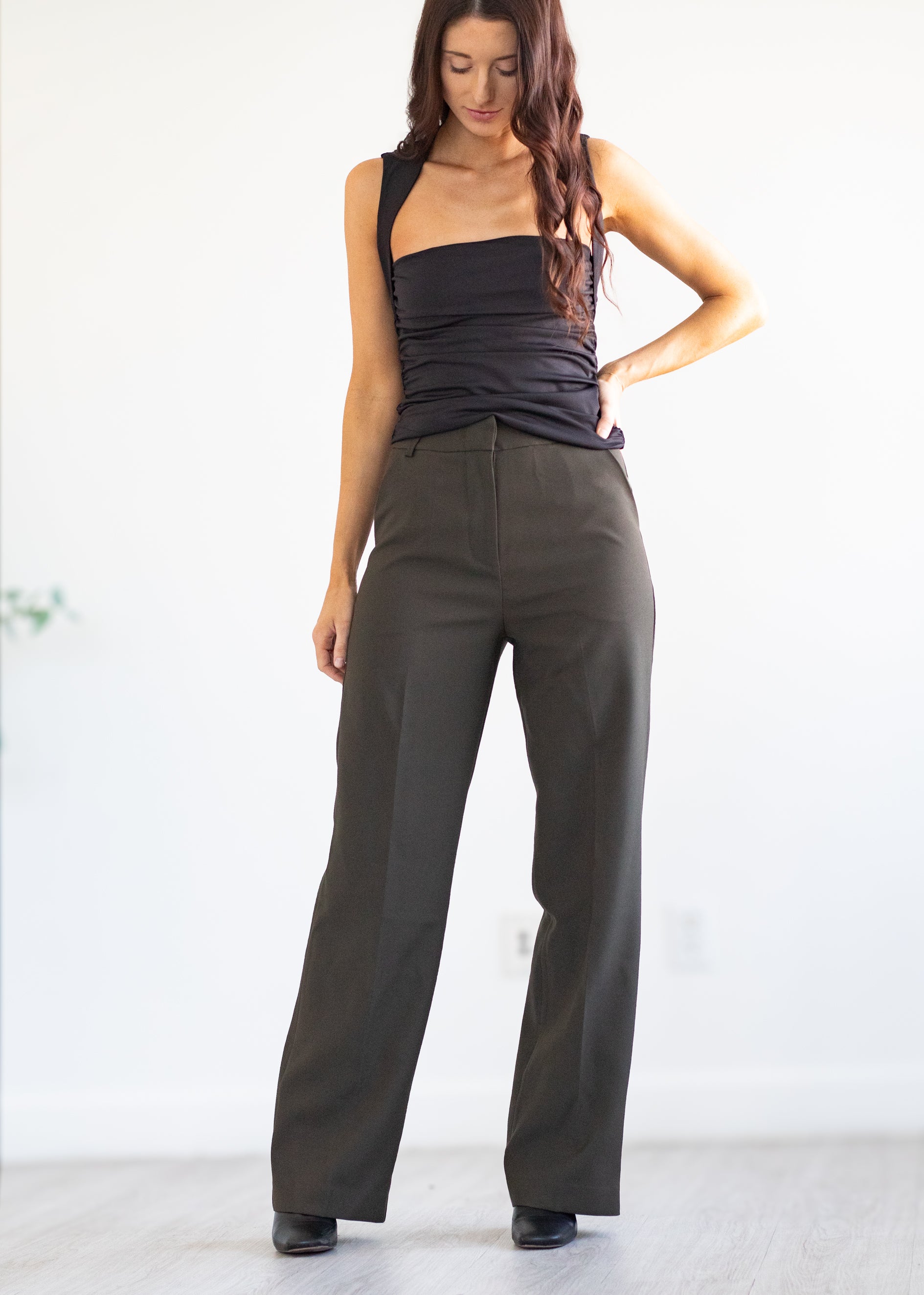 Woman wearing a black top and dark green pants on a white background