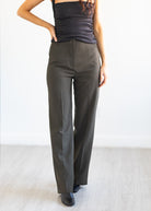 Person wearing olive green high-waisted pants and a black top on a white background