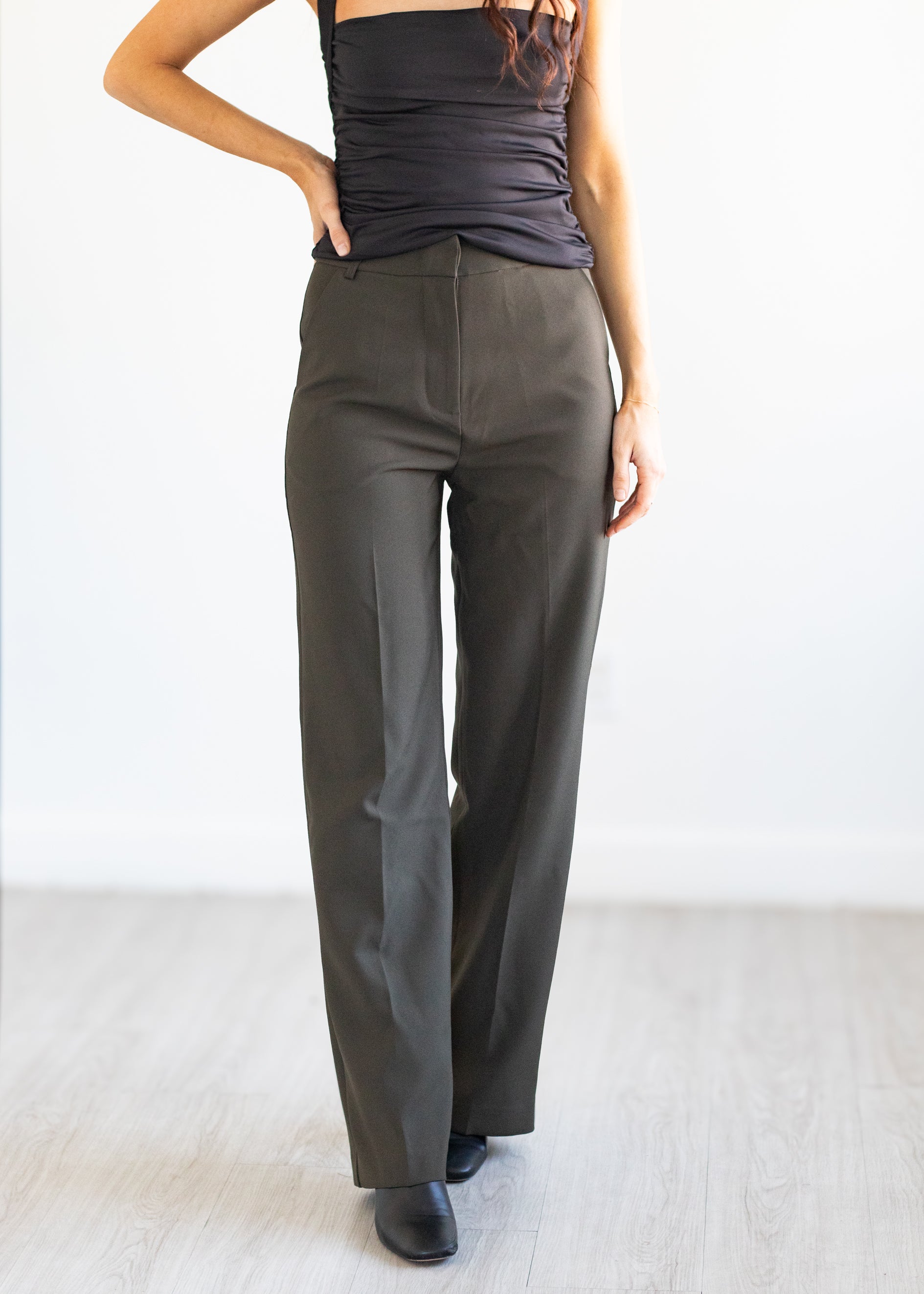 Person wearing olive green high-waisted pants and a black top on a white background