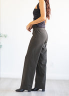 Woman wearing grey/green wide-leg pants and a black top against a white background