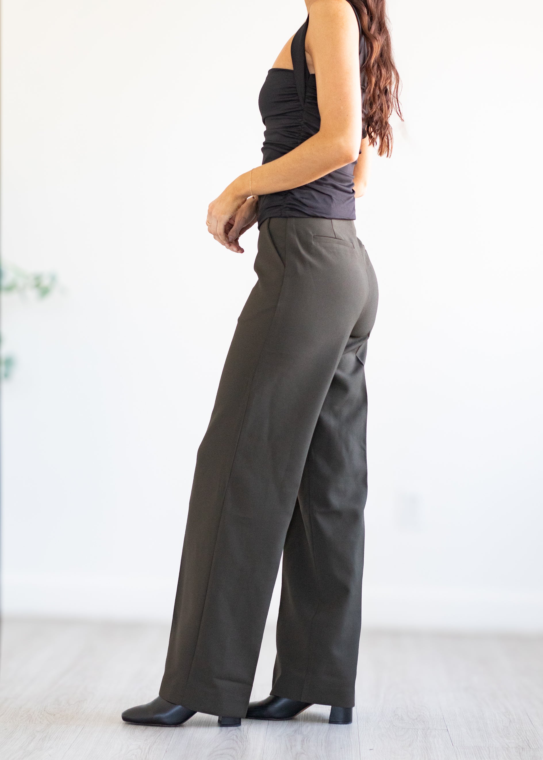 Woman wearing grey/green wide-leg pants and a black top against a white background
