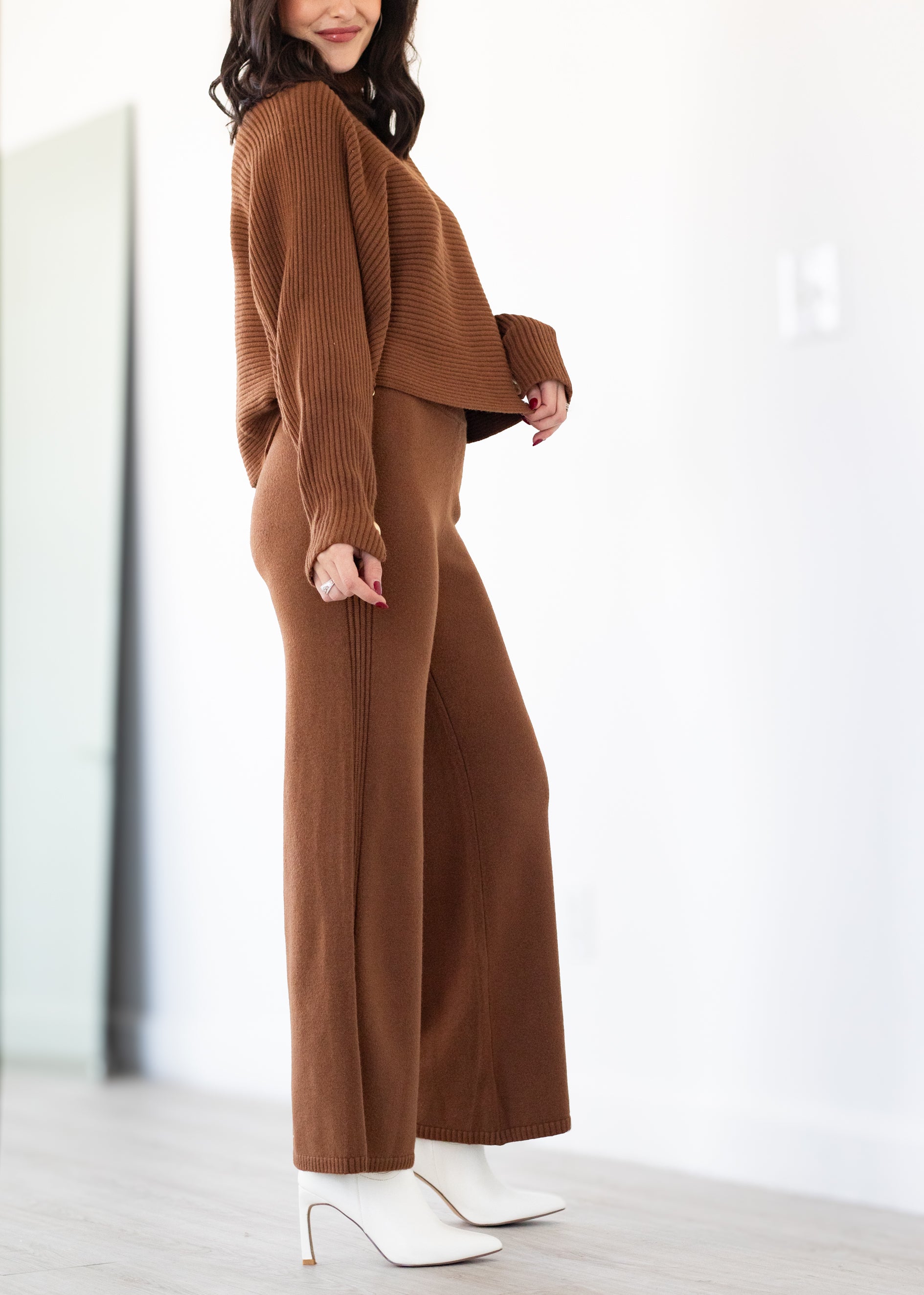 Woman wearing a brown ribbed sweater and wide-leg pants with white shoes on a light background