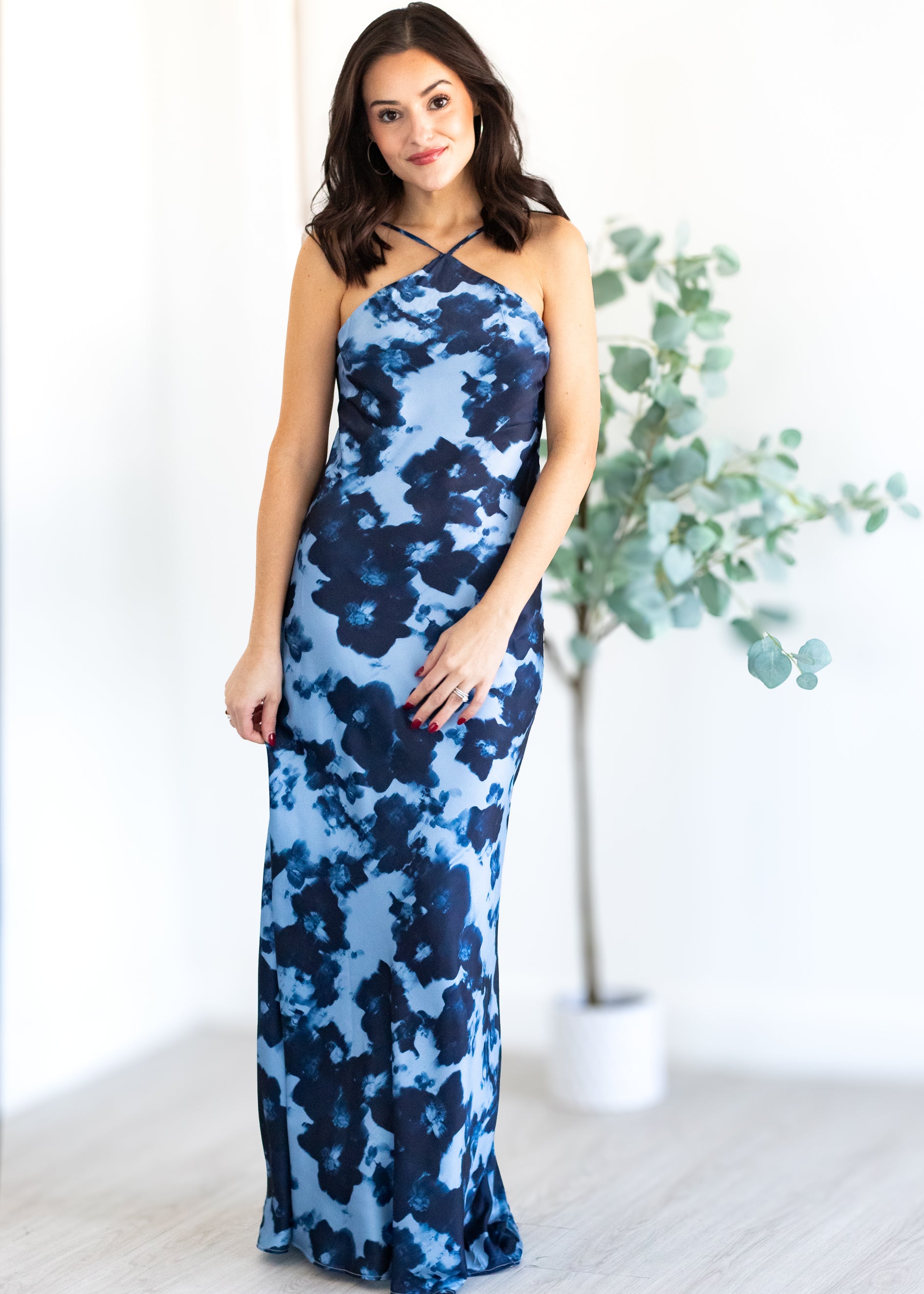 Woman wearing a blue floral dress standing in a room with a plant.