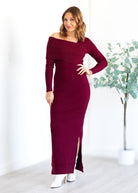 Woman wearing a burgundy off-shoulder dress with a slit, standing against a white background.
