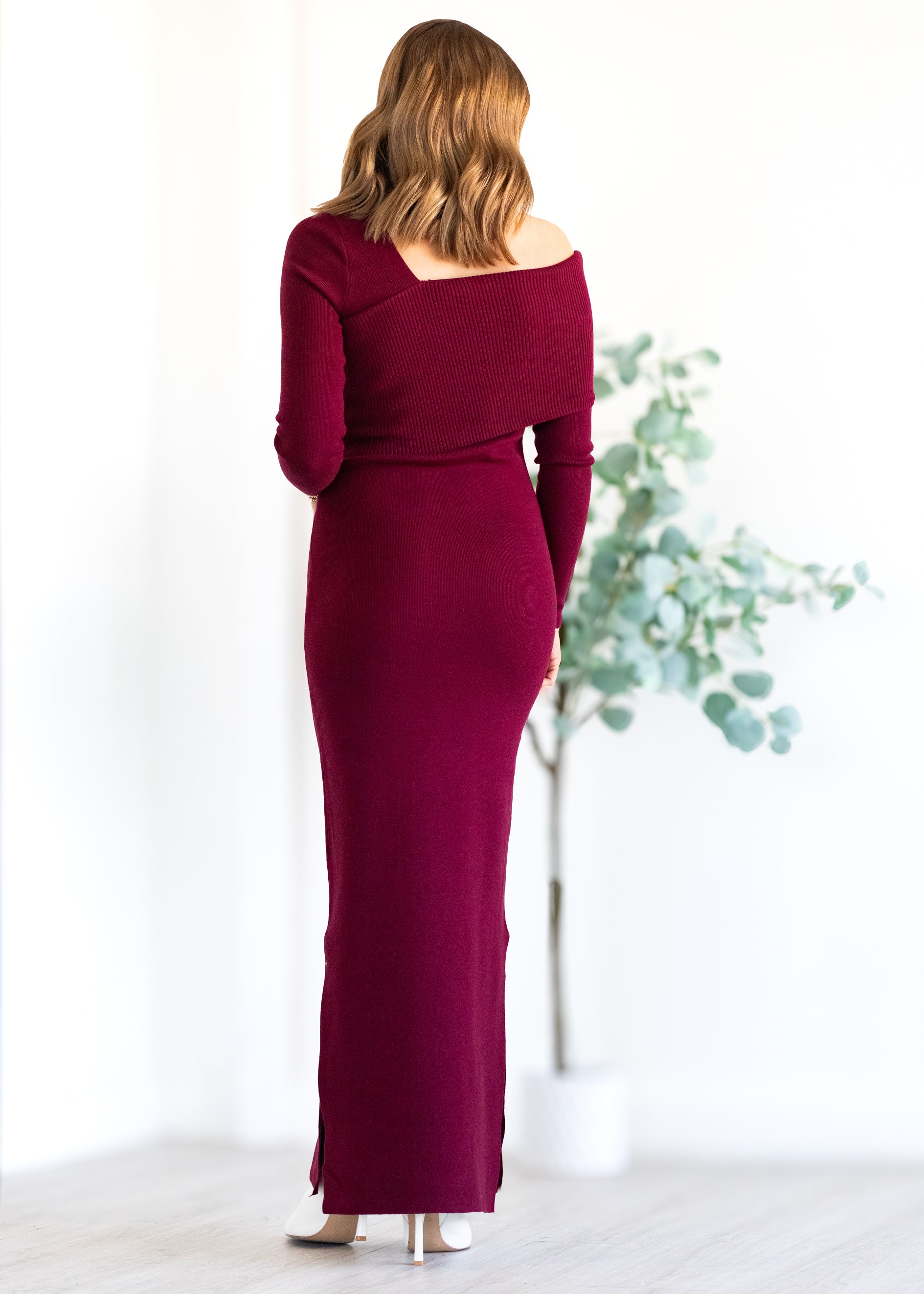 Woman wearing a burgundy off-shoulder dress with long sleeves, standing against a white background.