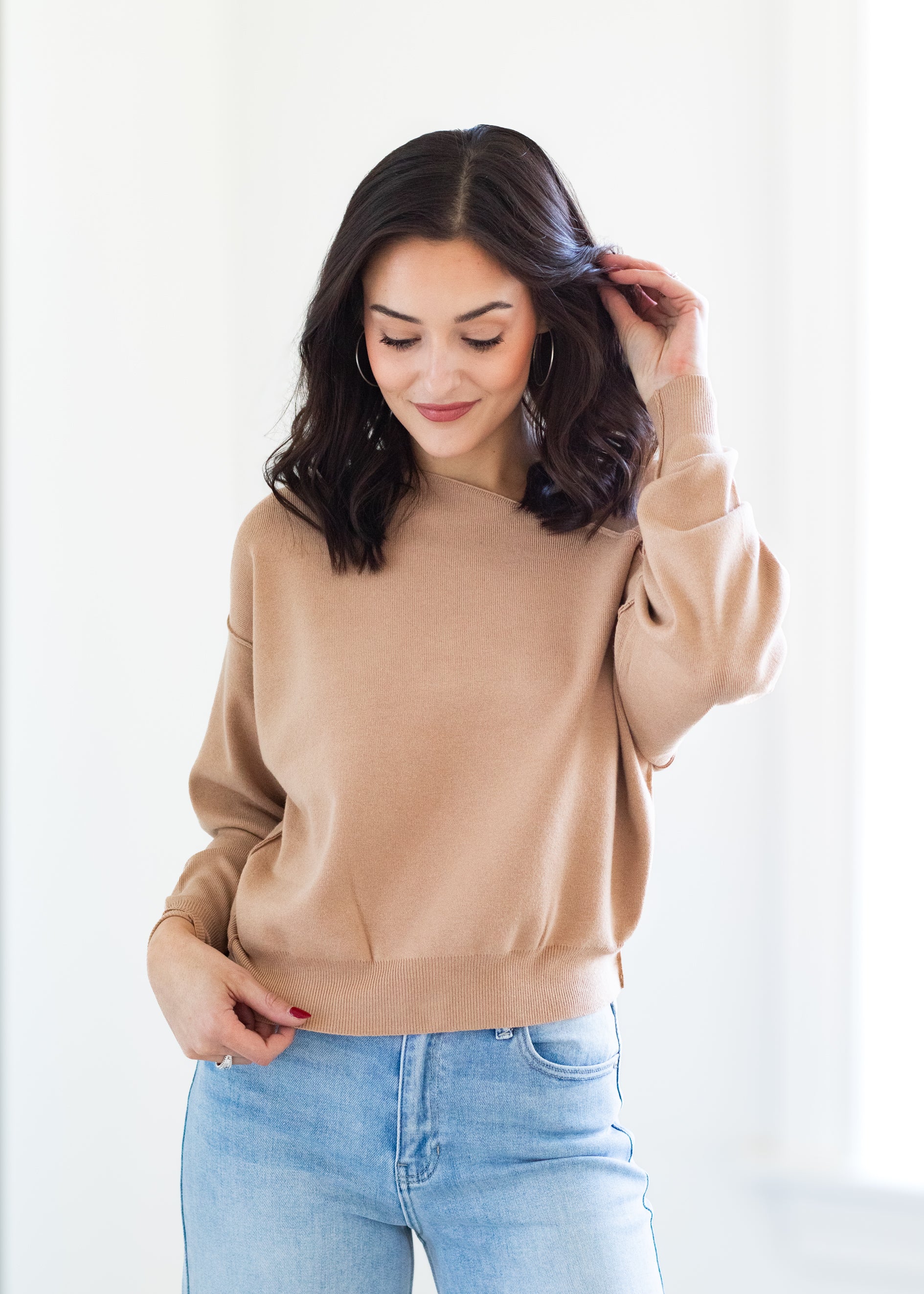 Woman wearing a beige sweater and light blue jeans against a white background