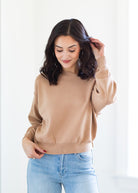 Woman wearing a beige sweater and light blue jeans against a white background