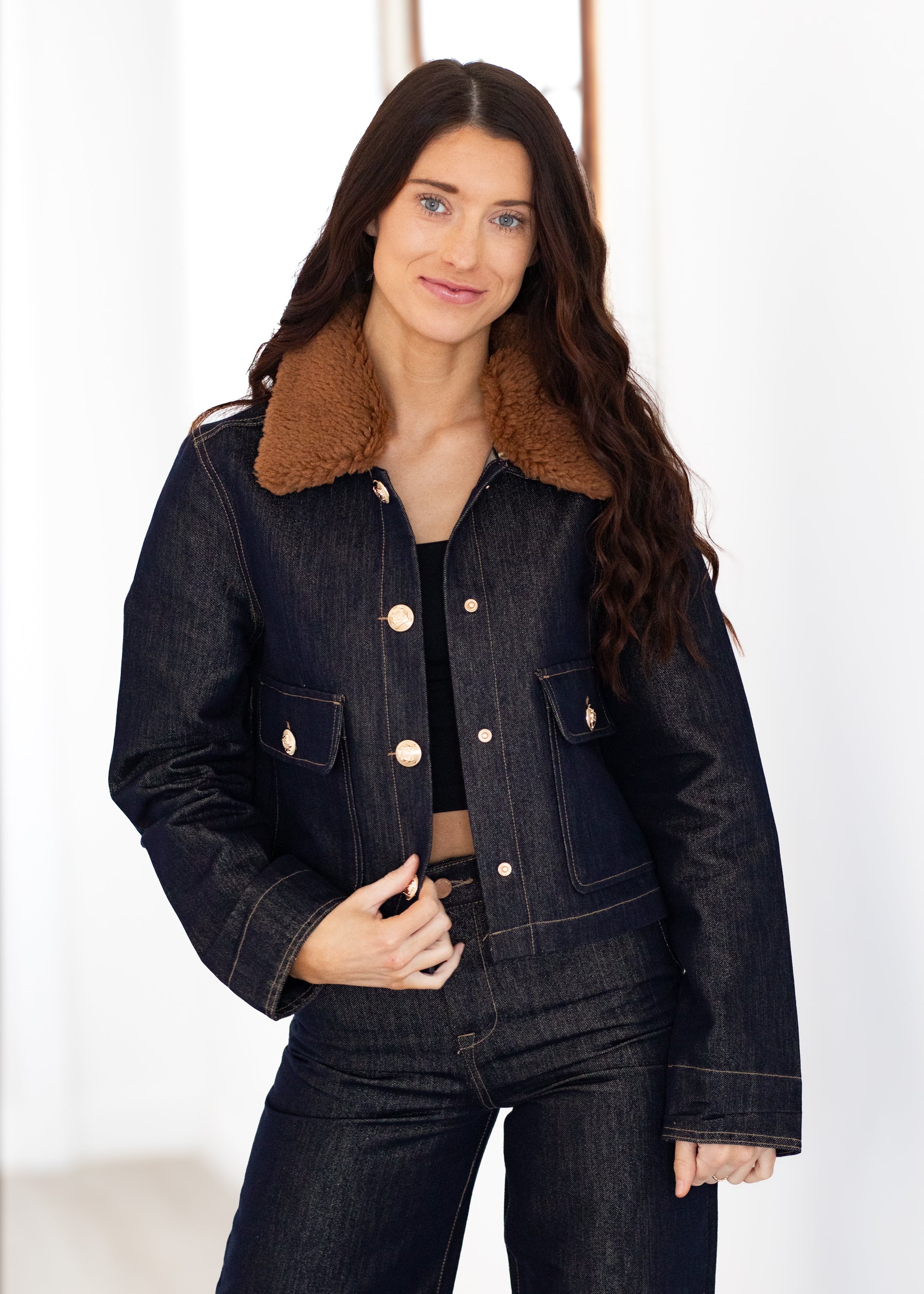 Woman wearing a dark denim jacket with brown fur collar against a white background
