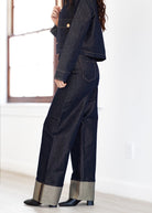 Person wearing a dark denim outfit with wide-leg pants and a cropped jacket in a minimalistic setting.