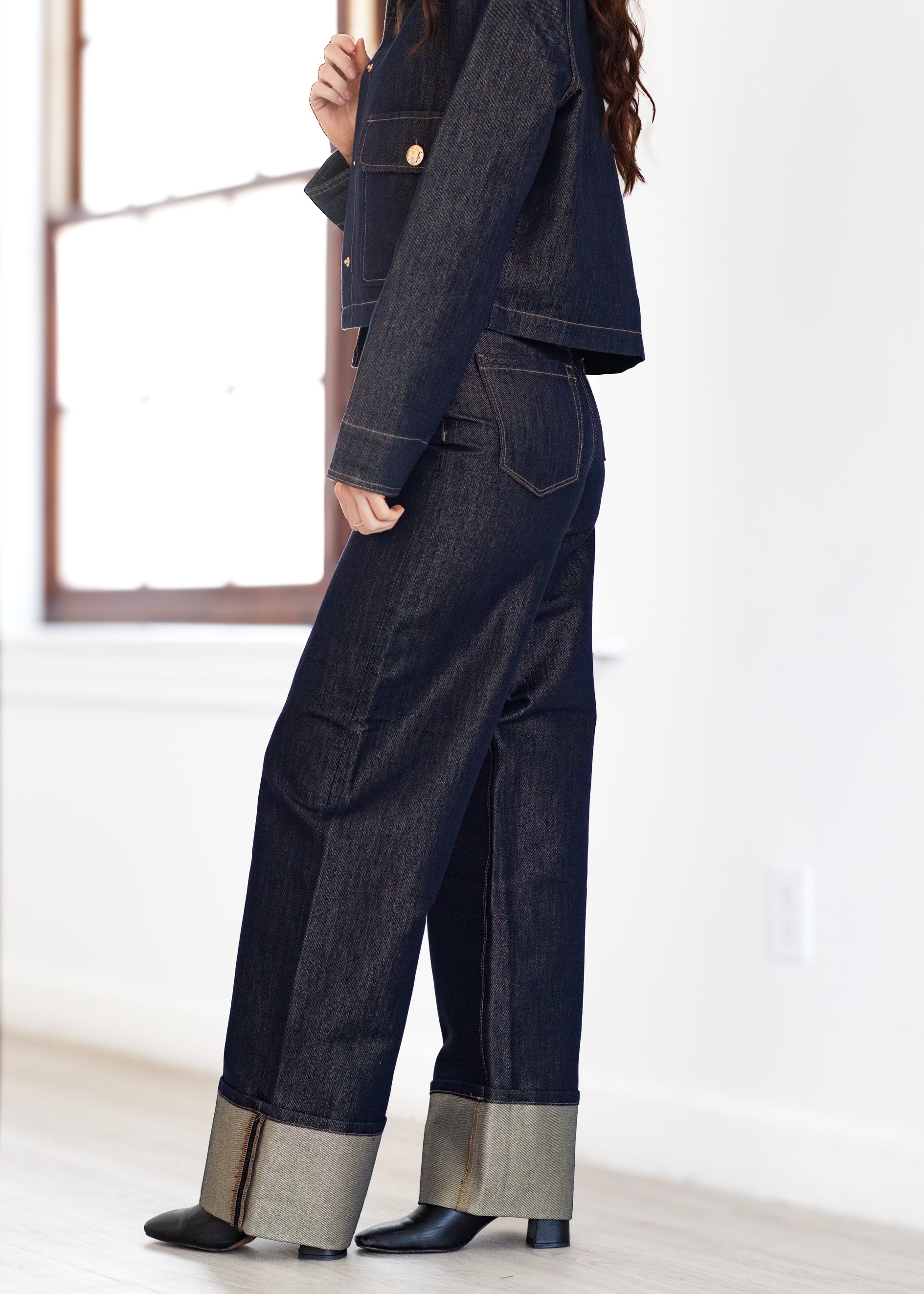 Person wearing a dark denim outfit with wide-leg pants and a cropped jacket in a minimalistic setting.