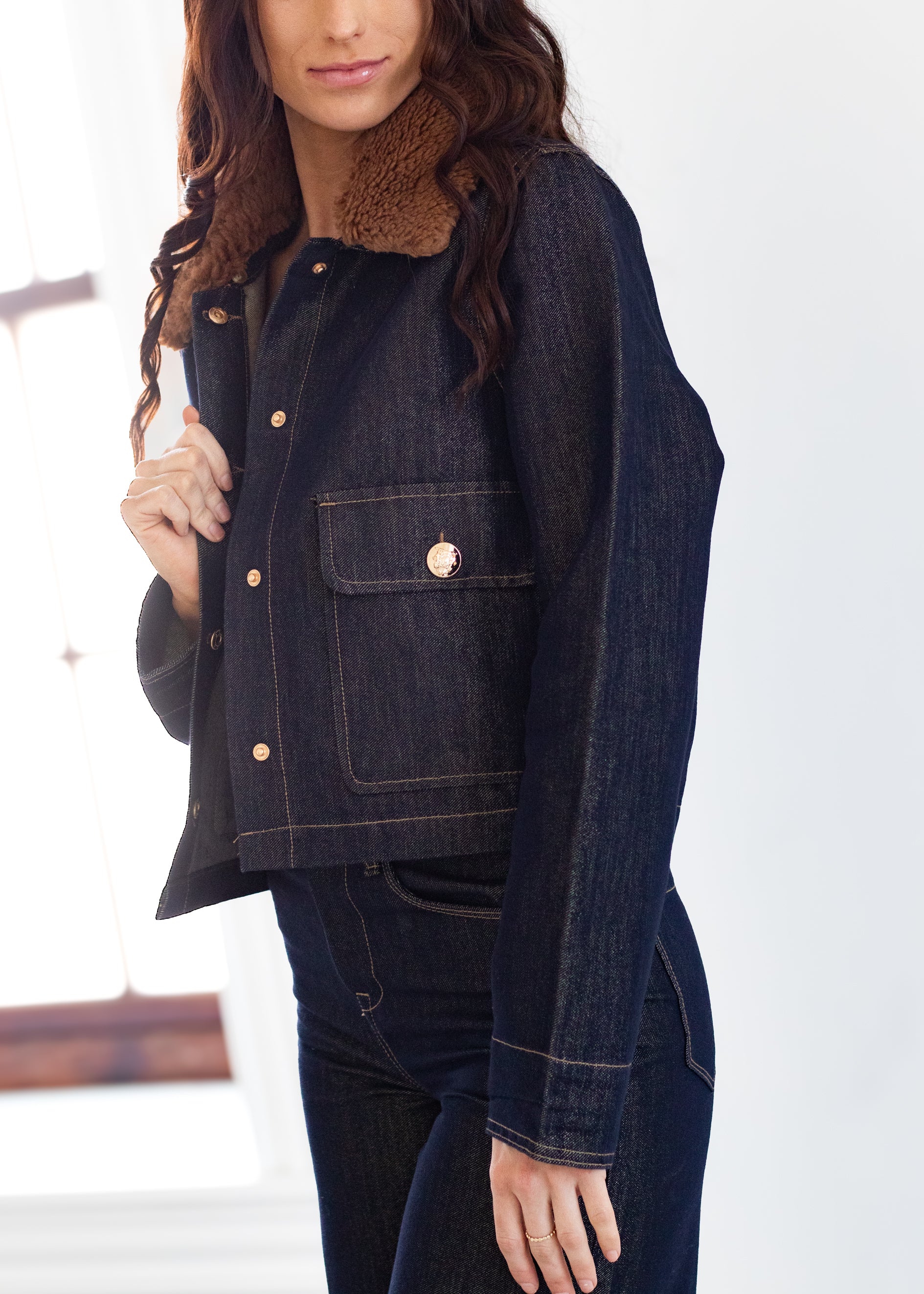 Person wearing a dark denim jacket with a fur collar against a white background