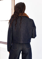 Person wearing a denim jacket with a fur-lined collar in a snowy landscape