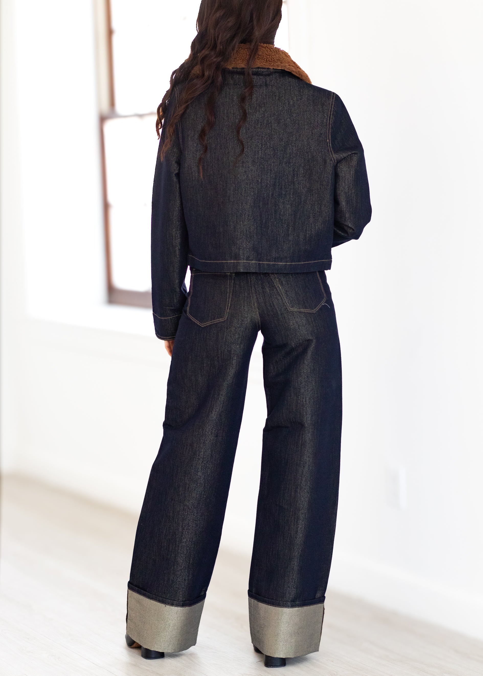 Person wearing a dark denim outfit with wide-leg pants on a white background